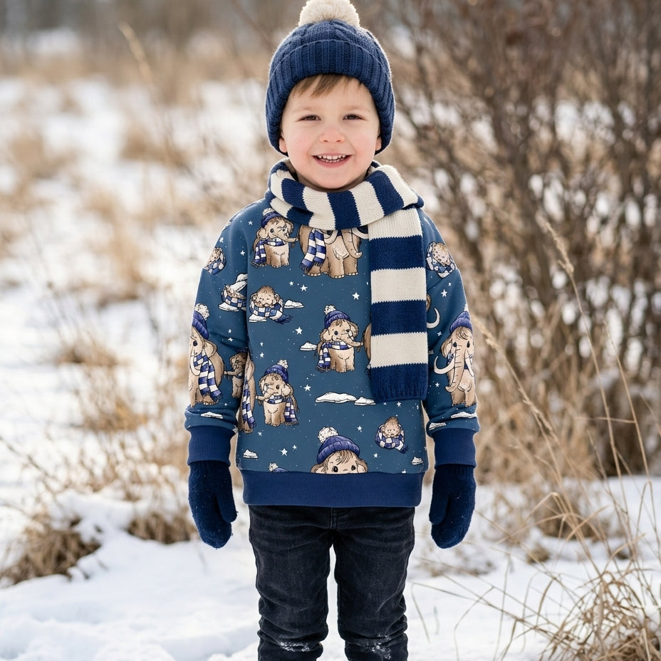 Kind im Schnee trägt selbstgenähten Pullover aus dem Stoff MammutBande in Jeansblau mit Mammut-Motiv